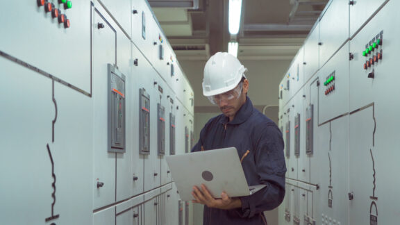 An engineer man or worker, people using a laptop computer, working in electrical room. Power energy motor machinery cabinets in control or server room, operator station network in industry factory.
