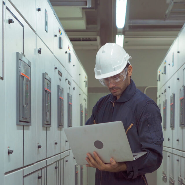 An engineer man or worker, people using a laptop computer, working in electrical room. Power energy motor machinery cabinets in control or server room, operator station network in industry factory.